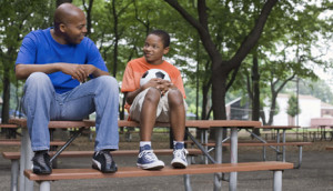 Man and boy sitting on picnic table with soccer ball